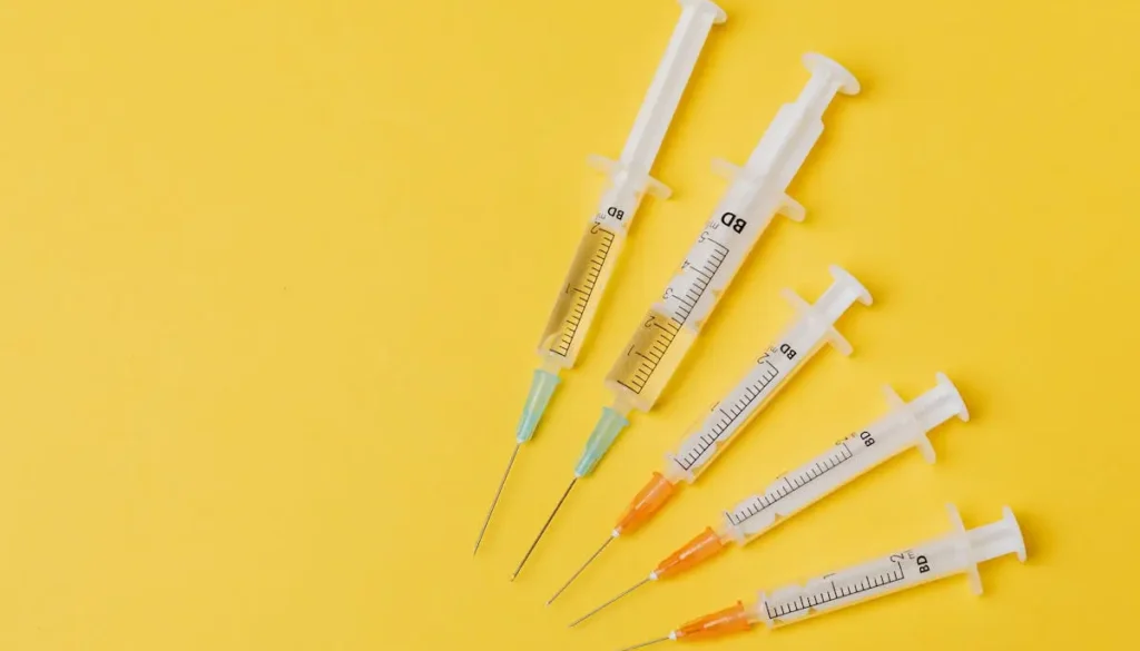 Four syringes positioned on a yellow surface, emphasizing their transparent design and colorful needle ends.