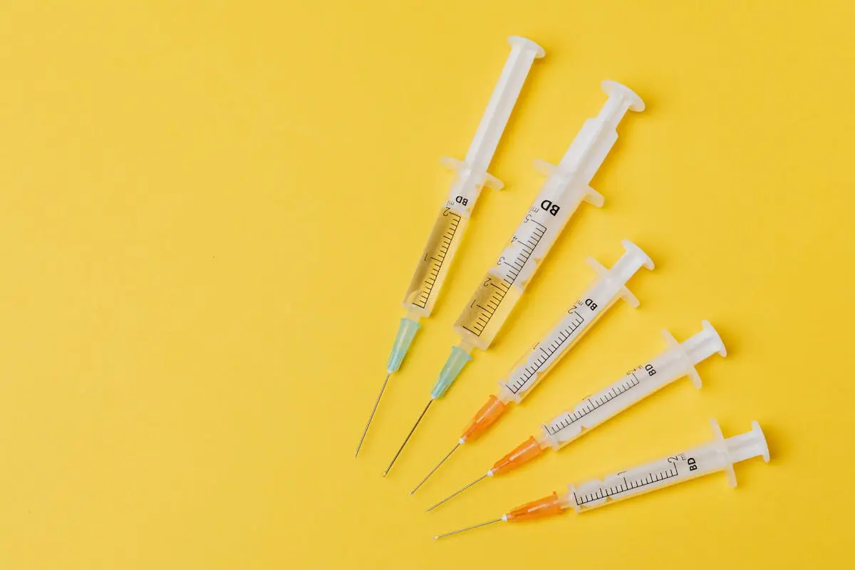 Four syringes positioned on a yellow surface, emphasizing their transparent design and colorful needle ends.