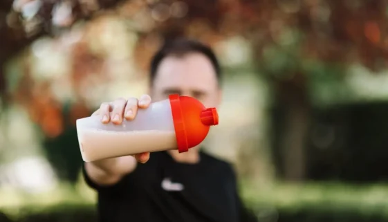 A man grips a pre-workout shake bottle, symbolizing his dedication to health and fitness.