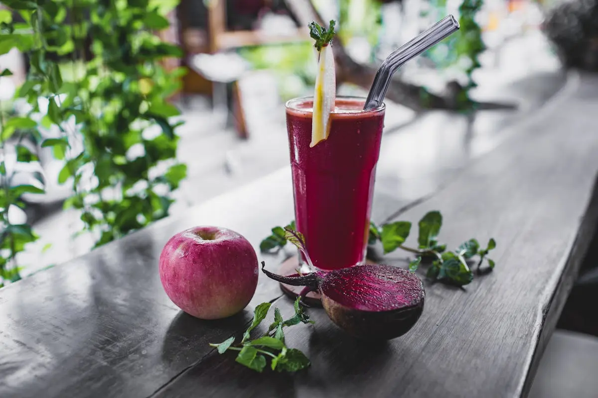 A glass of vibrant juice accompanied by a fresh apple and a beetroot, showcasing a healthy beverage choice